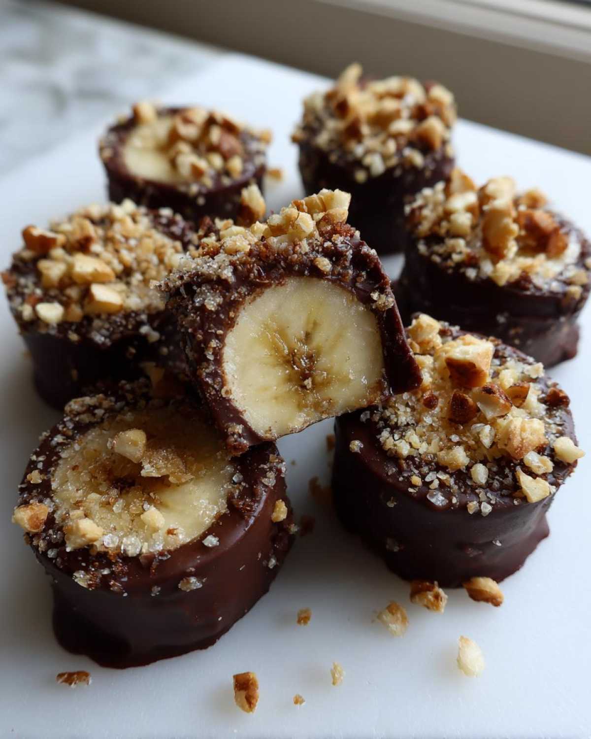 Close-up of several No-Bake Chocolate Covered Banana Bites topped with chopped nuts and sea salt.