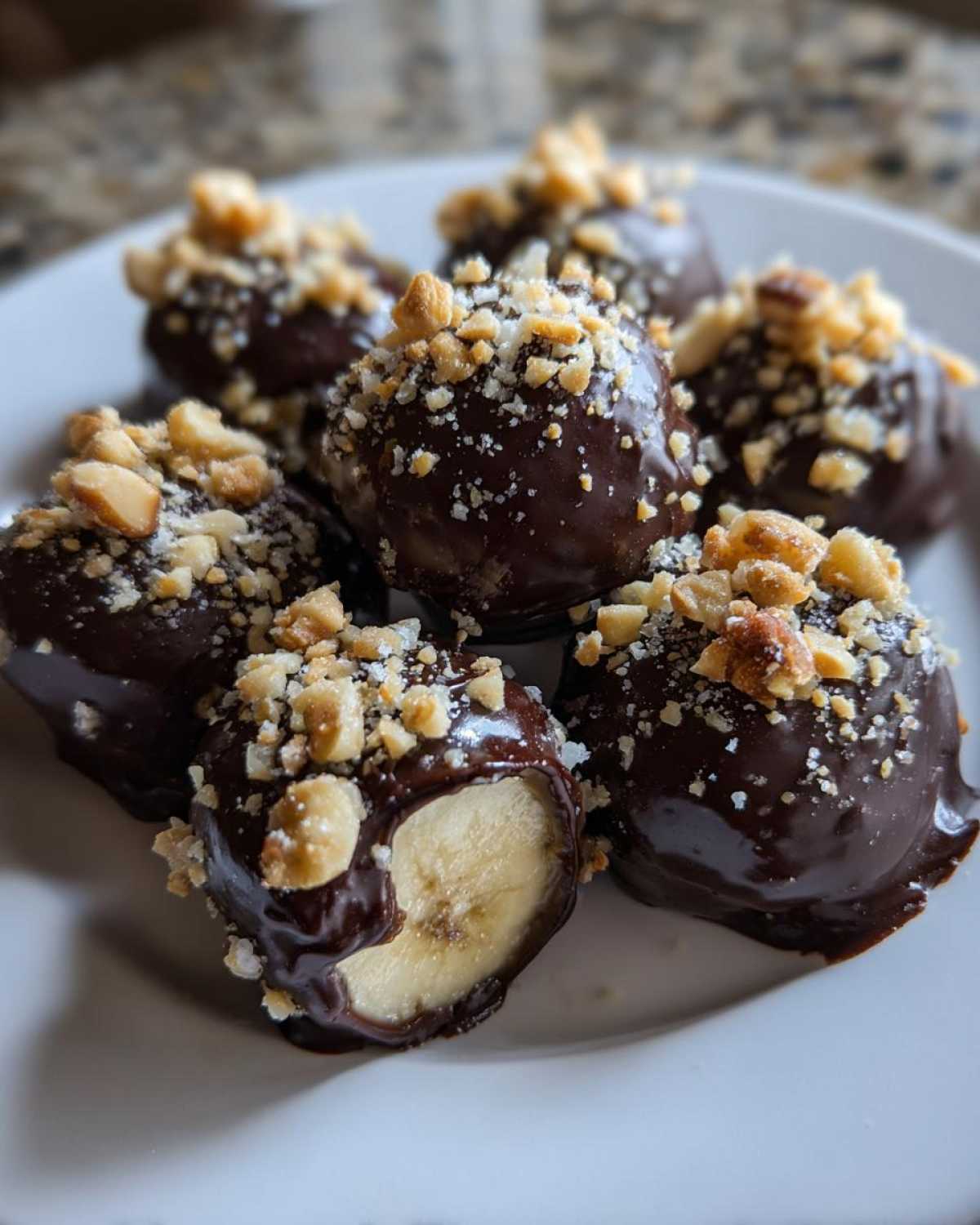 Close-up of several No-Bake Chocolate Covered Banana Bites topped with chopped nuts on a white plate.