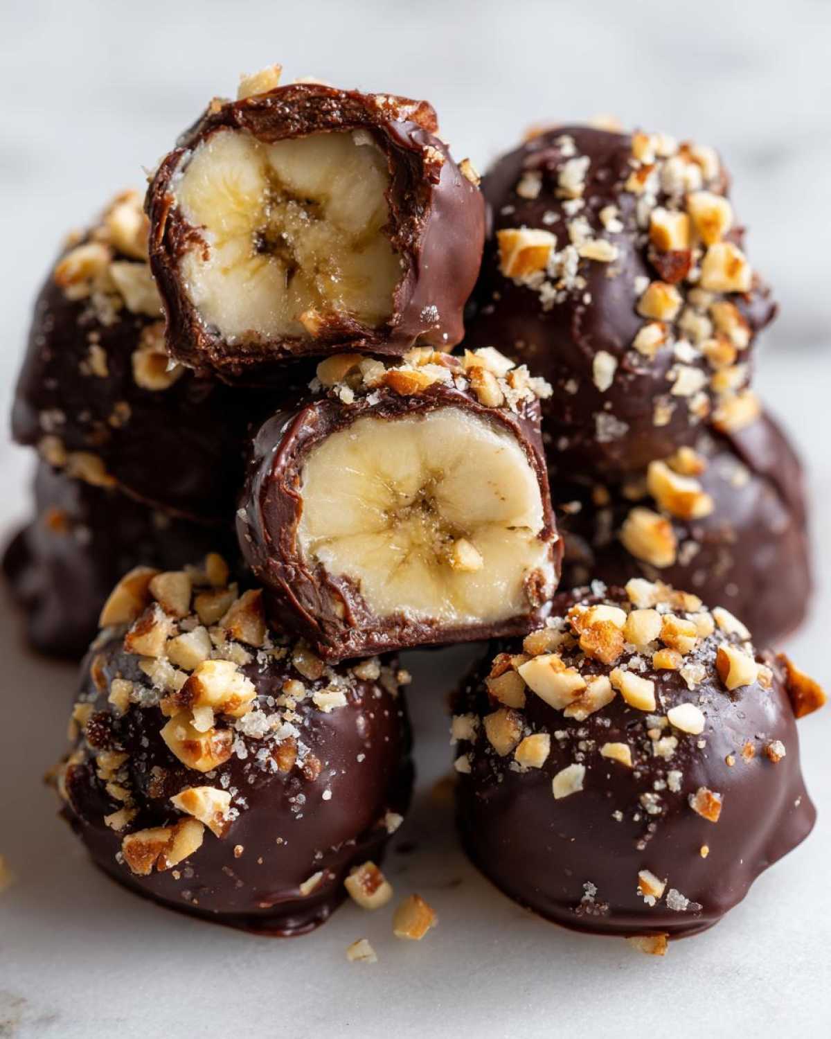 Stack of No-Bake Chocolate Covered Banana Bites dipped in dark chocolate and topped with chopped nuts.
