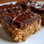 Close-up of thick, layered No-Bake Chocolate Peanut Butter Oat Bars with a shiny chocolate topping.