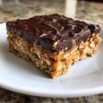 A square portion of No-Bake Chocolate Peanut Butter Oat Bars showing the oat base, gooey peanut butter layer, and rich chocolate topping.