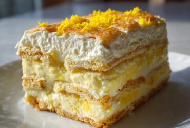 A tall slice of layered No-Bake Lemon Icebox Cake topped with whipped cream and bright yellow lemon zest.