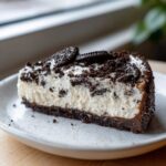 A close-up of a rich slice of No-Bake Oreo Cheesecake with a creamy white filling and dark chocolate cookie crust.
