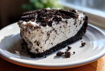 A thick slice of No-Bake Oreo Cheesecake with a creamy filling and dark crust, topped with crushed Oreos.