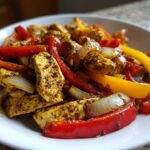 Close-up of seasoned chicken strips mixed with sliced red and yellow peppers and onions from One-Pan Chicken Fajitas.