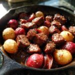Close-up of juicy steak bites and small red and yellow potatoes cooked in garlic butter in a cast iron skillet.
