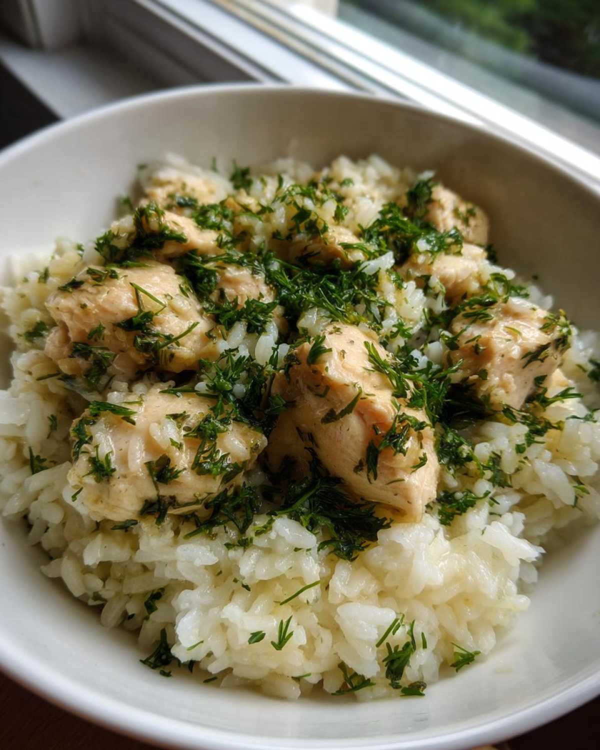 Close-up of a white bowl filled with One-Pot Chicken and Rice with Lemon and Herbs, topped generously with fresh green herbs.