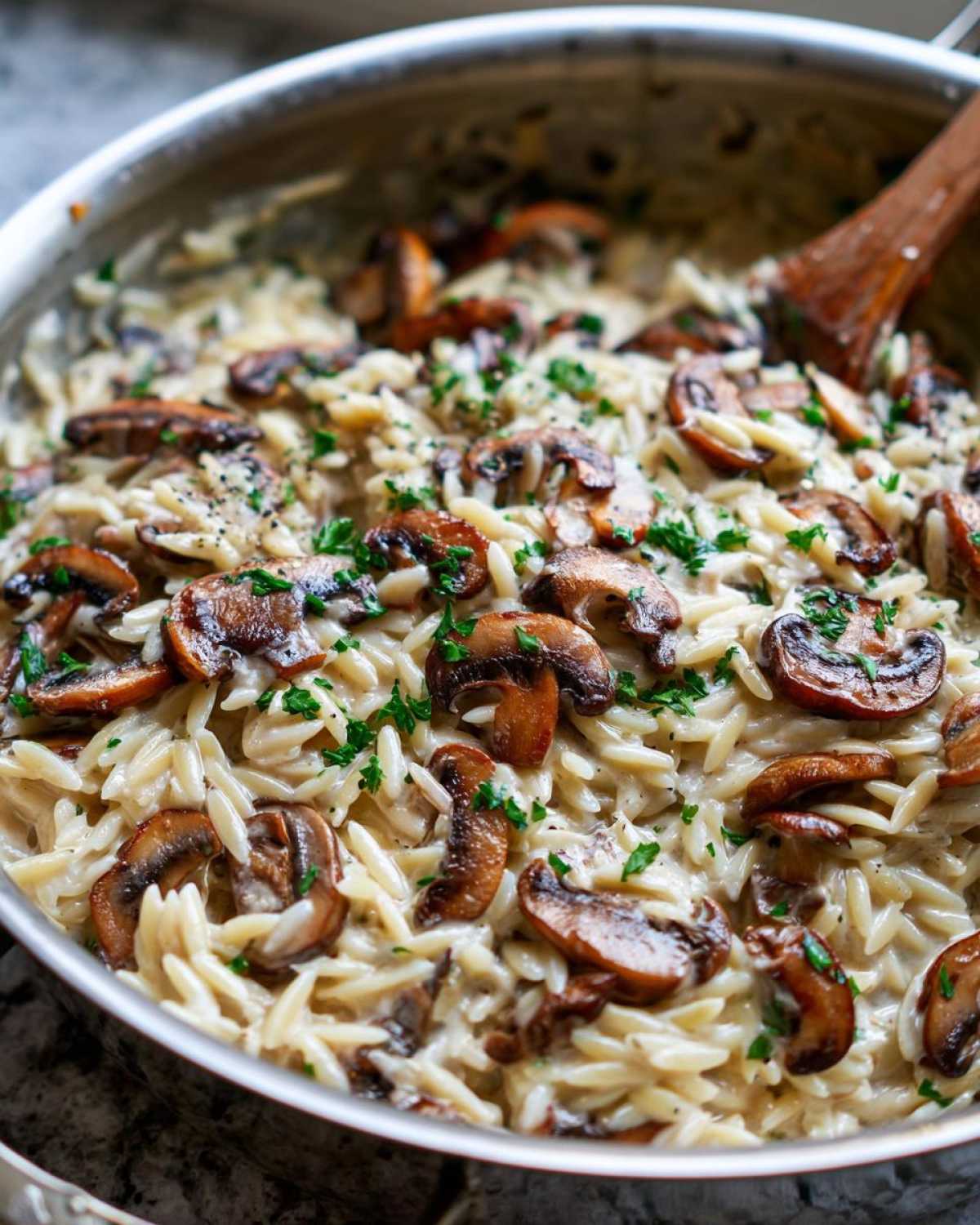 Close-up shot of One-Pot Creamy Mushroom Orzo topped with sautéed mushrooms and parsley in a stainless steel skillet.