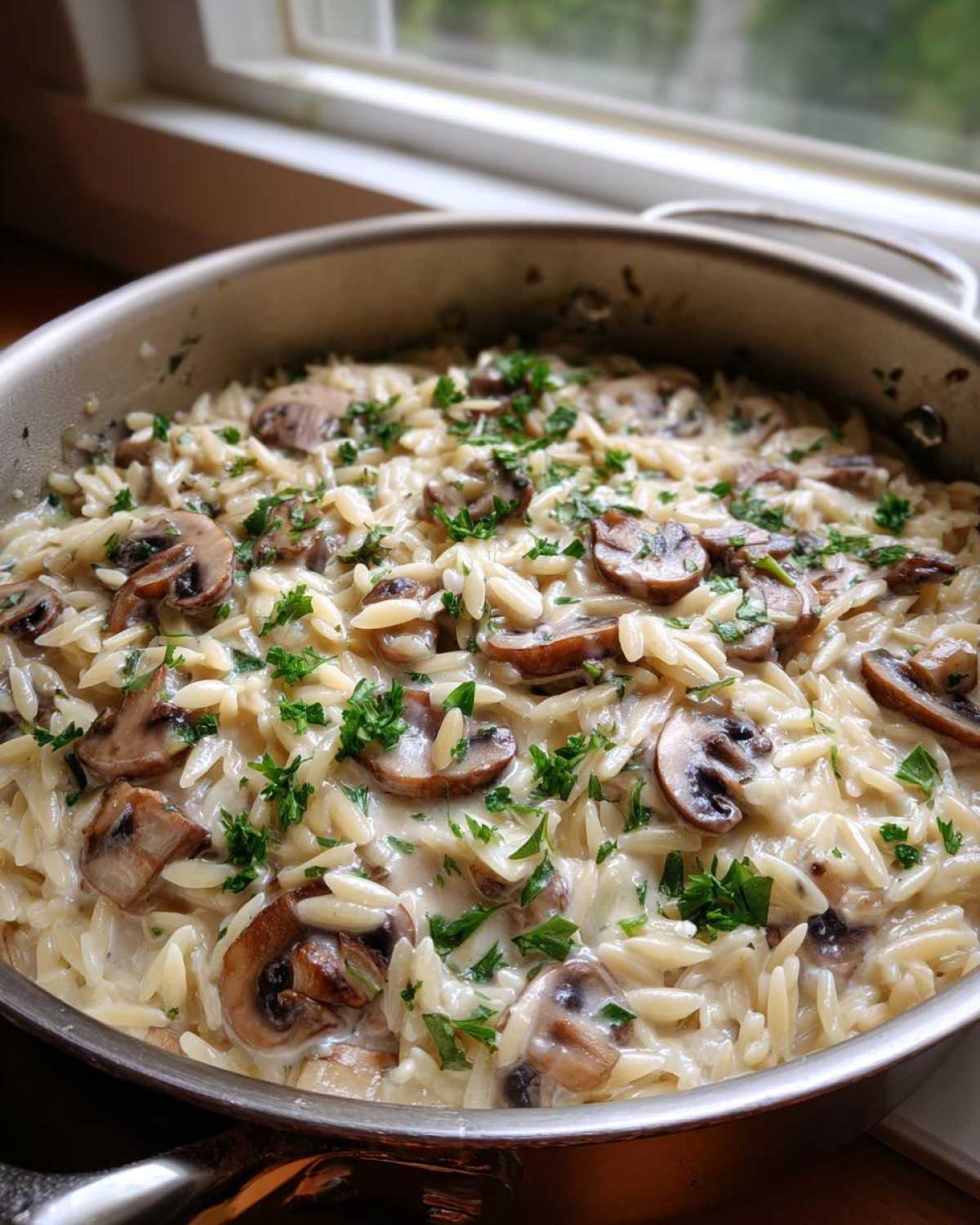 A stainless steel skillet filled with creamy One-Pot Creamy Mushroom Orzo, topped with sliced mushrooms and fresh parsley.