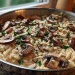 Close-up of creamy One-Pot Creamy Mushroom Orzo topped with sautéed mushrooms and parsley in a stainless steel skillet.