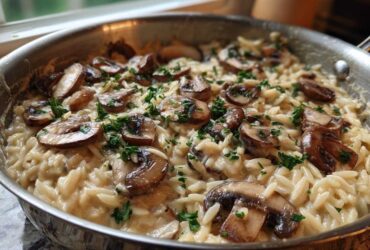Close-up of creamy One-Pot Creamy Mushroom Orzo topped with sautéed mushrooms and parsley in a stainless steel skillet.