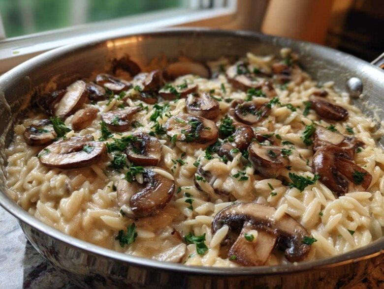 Close-up of creamy One-Pot Creamy Mushroom Orzo topped with sautéed mushrooms and parsley in a stainless steel skillet.