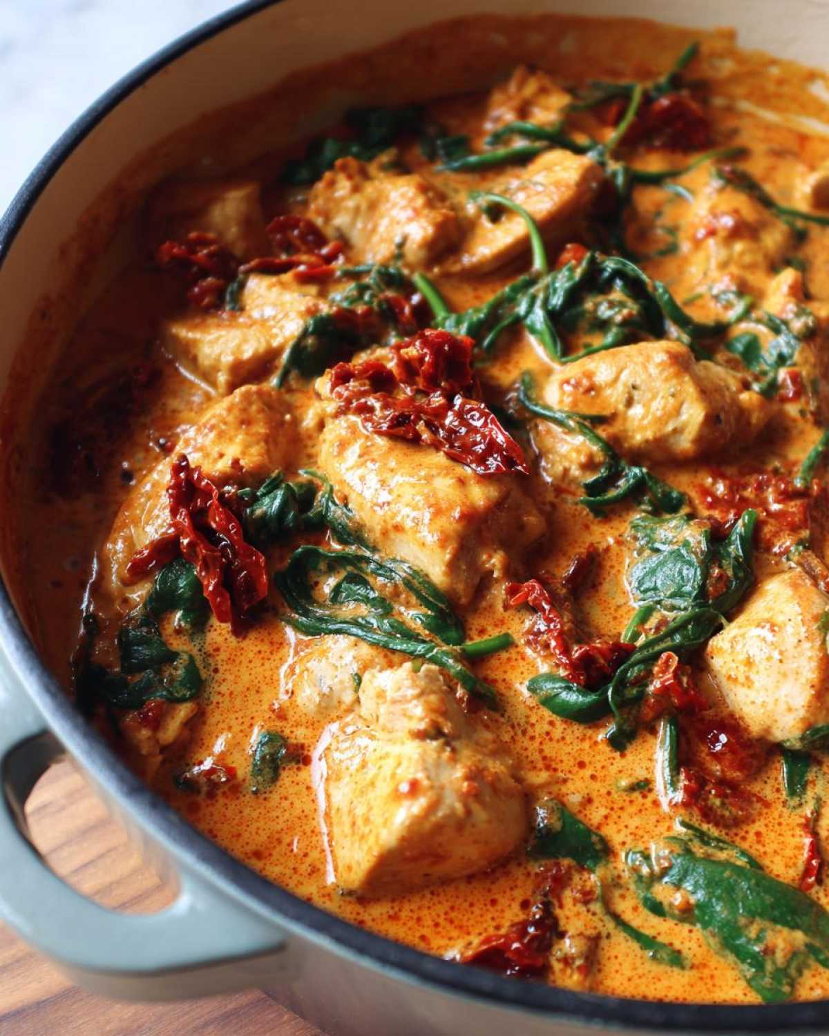 Close-up of One-Pot Creamy Sun-Dried Tomato Chicken with spinach in a light green Dutch oven.