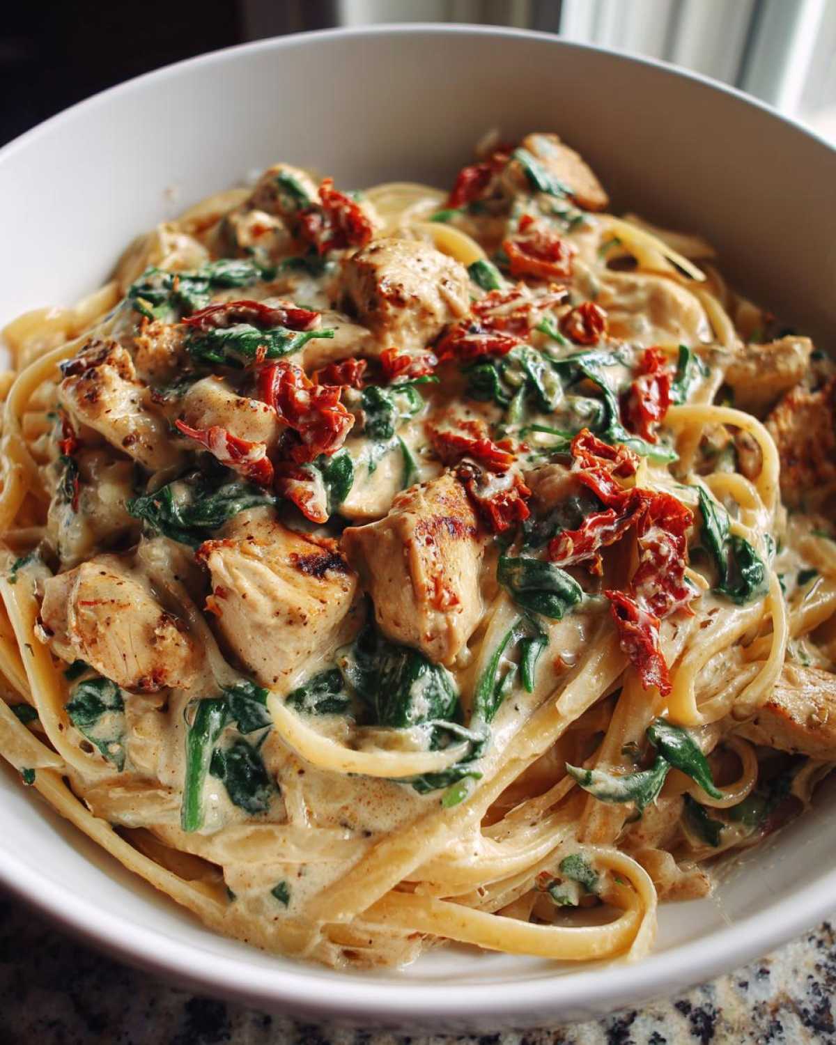 Close-up of One-Pot Creamy Tuscan Chicken Pasta featuring linguine, grilled chicken pieces, spinach, and sun-dried tomatoes in a rich cream sauce.