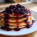 A stack of fluffy pancakes generously topped with thick, rich Homemade Blueberry Syrup and whole berries.