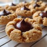 Close-up of a freshly baked Peanut Butter Blossom Cookie with a chocolate kiss center cooling on a wire rack.