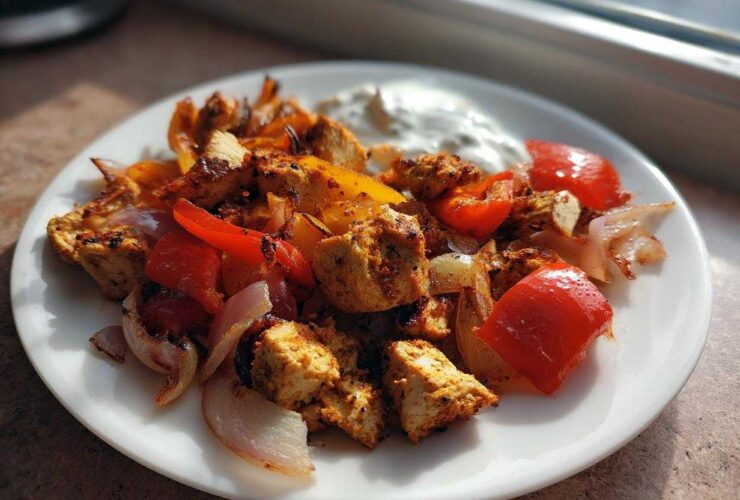 A plate of Sheet Pan Chicken Shawarma mixed with roasted red peppers and onions, served with a dollop of garlic yogurt sauce.