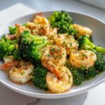 Close-up of cooked shrimp and bright green broccoli florets tossed in garlic butter seasoning.
