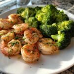 Cooked shrimp coated in garlic butter and parsley served next to bright green broccoli florets.