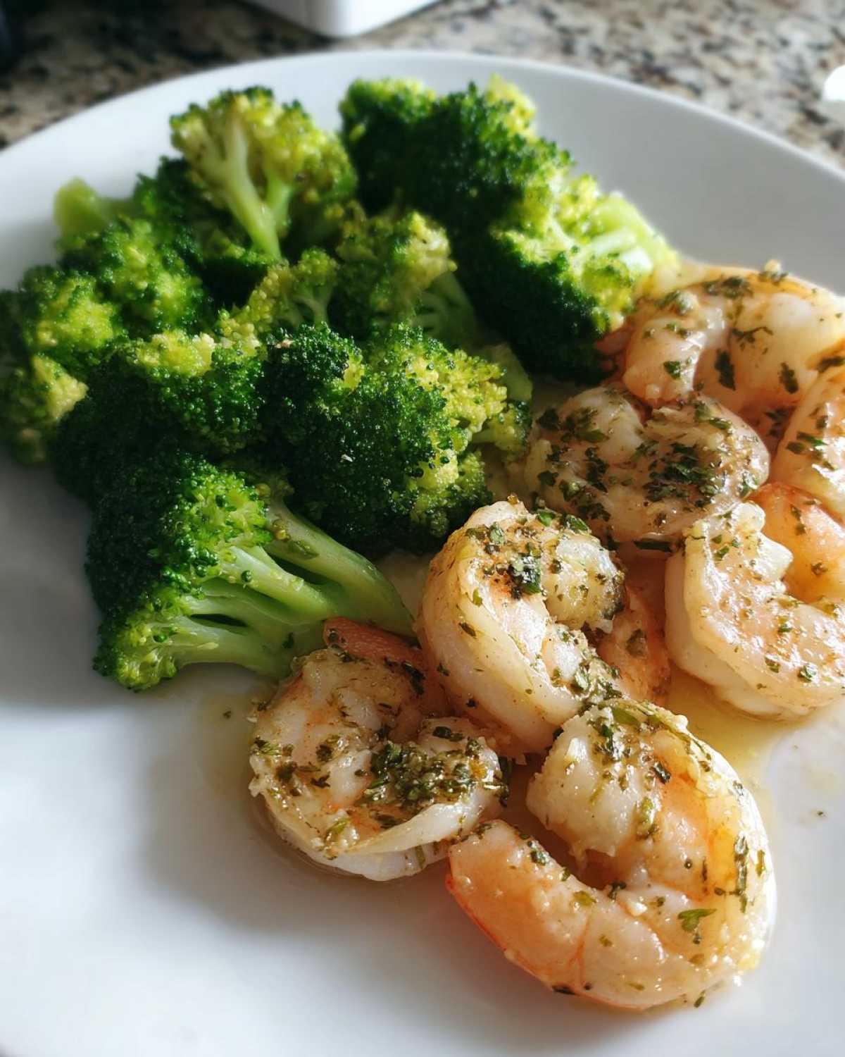 A plate featuring cooked shrimp coated in garlic butter sauce next to bright green broccoli florets, part of the Sheet Pan Garlic Butter Shrimp and Broccoli recipe.