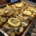 Close-up of Sheet Pan Lemon Pepper Chicken and Potatoes seasoned with herbs and topped with lemon slices.