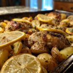 Close-up of Sheet Pan Lemon Pepper Chicken and Potatoes topped with lemon slices and herbs.