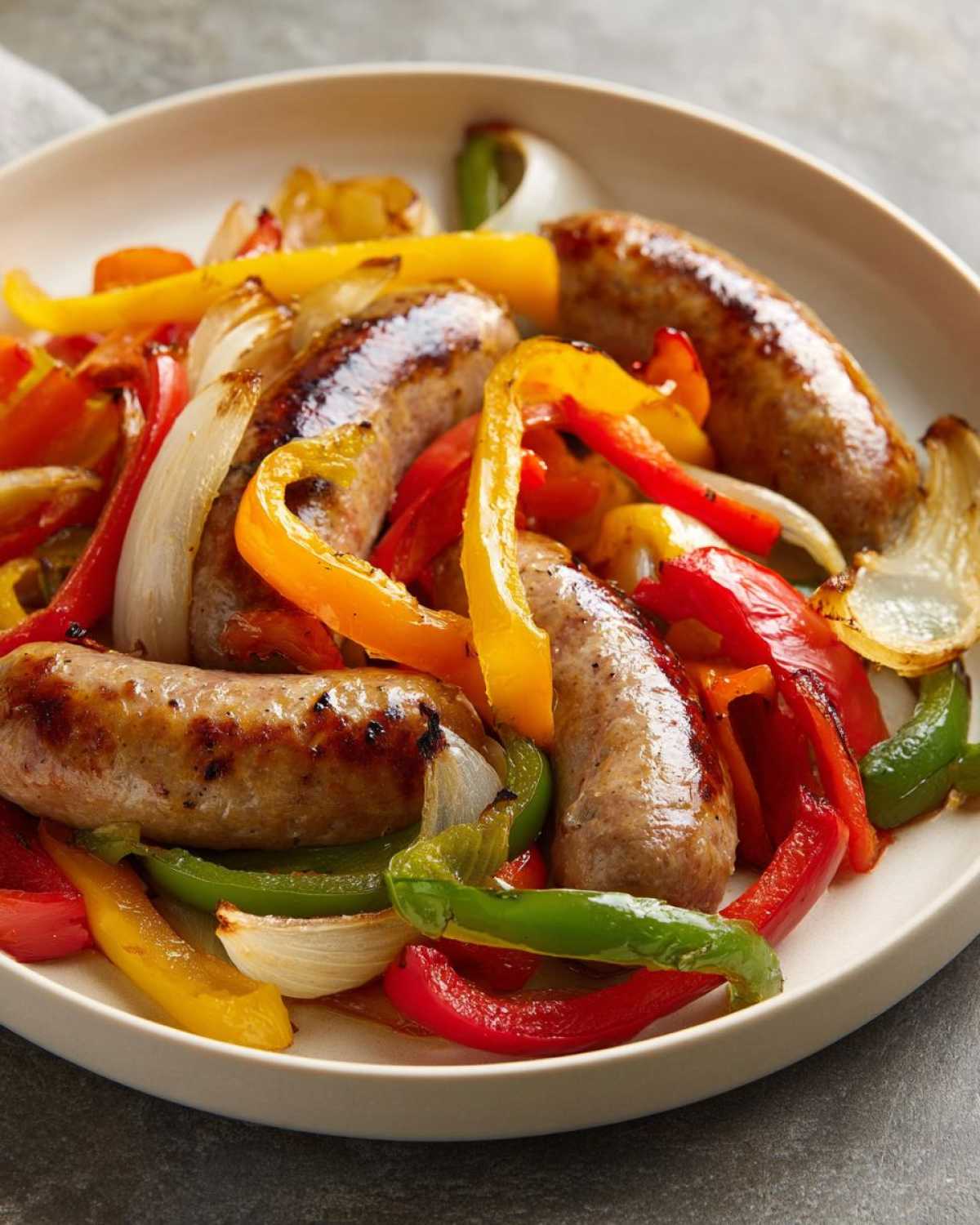 Close-up of perfectly cooked Sheet Pan Sausage and Peppers with caramelized onions on a light-colored plate.