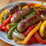 Close-up of browned sausages served over colorful roasted peppers and onions from a Sheet Pan Sausage and Peppers recipe.
