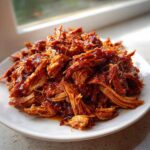 A close-up of shredded Slow Cooker Honey Garlic Pulled Pork piled high on a white plate, glistening with sauce.