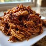 A close-up of shredded, saucy Slow Cooker Honey Garlic Pulled Pork piled high on a white plate.