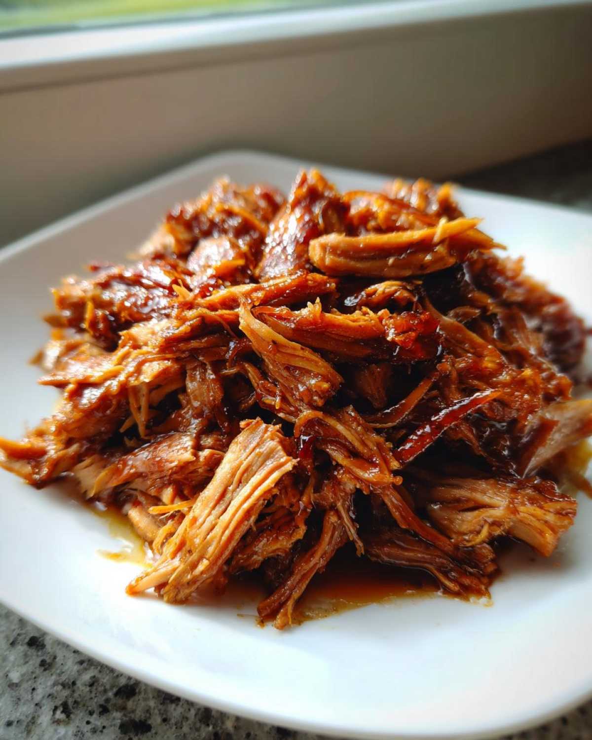 Close-up of tender, shredded Slow Cooker Honey Garlic Pulled Pork coated in a rich, glossy sauce on a white plate.