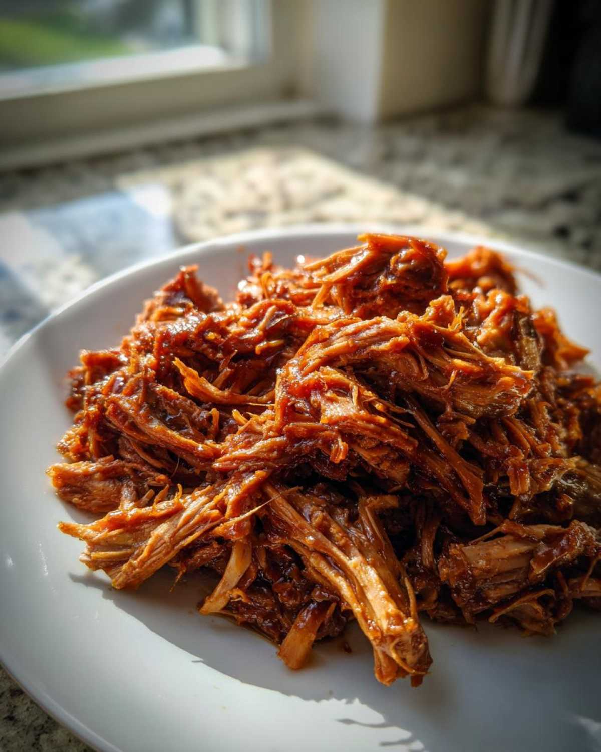 Close-up of shredded, saucy Slow Cooker Honey Garlic Pulled Pork piled high on a white plate.