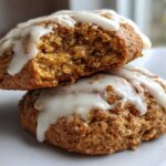 Two stacked Soft-Baked Carrot Cake Cookies topped with dripping cream cheese glaze, one cookie is broken open.