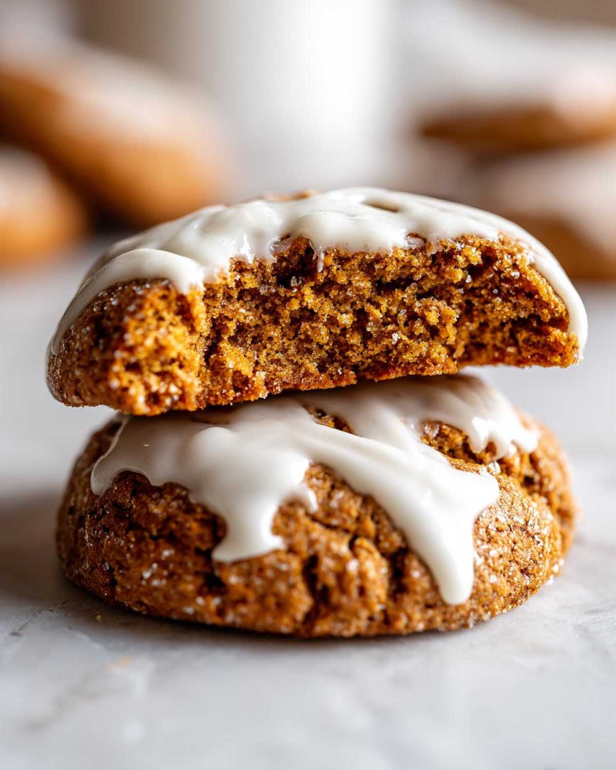 Two stacked Soft-Baked Carrot Cake Cookies, one broken open to show the soft interior and thick cream cheese glaze.