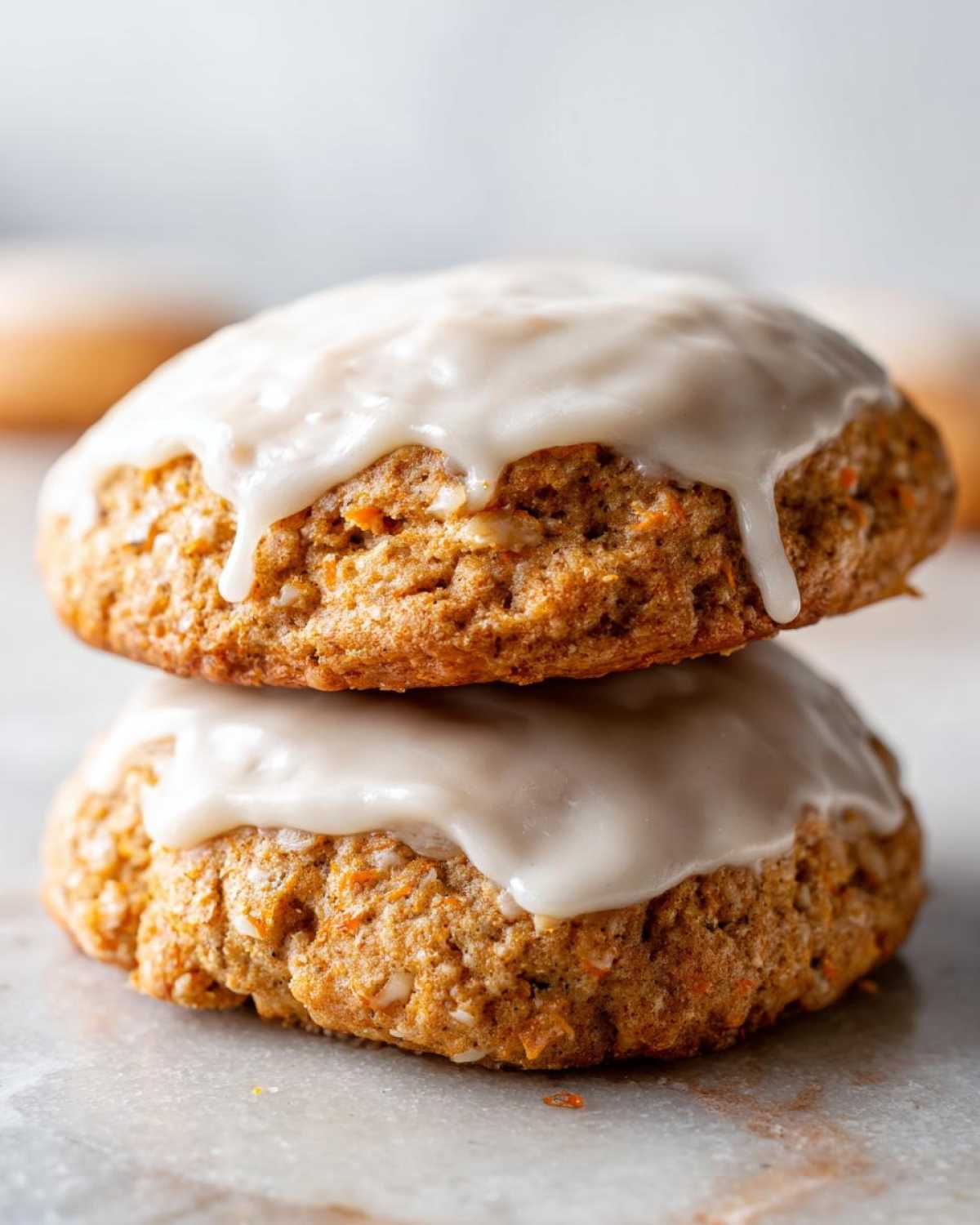 Two stacked Soft-Baked Carrot Cake Cookies topped with dripping cream cheese glaze.