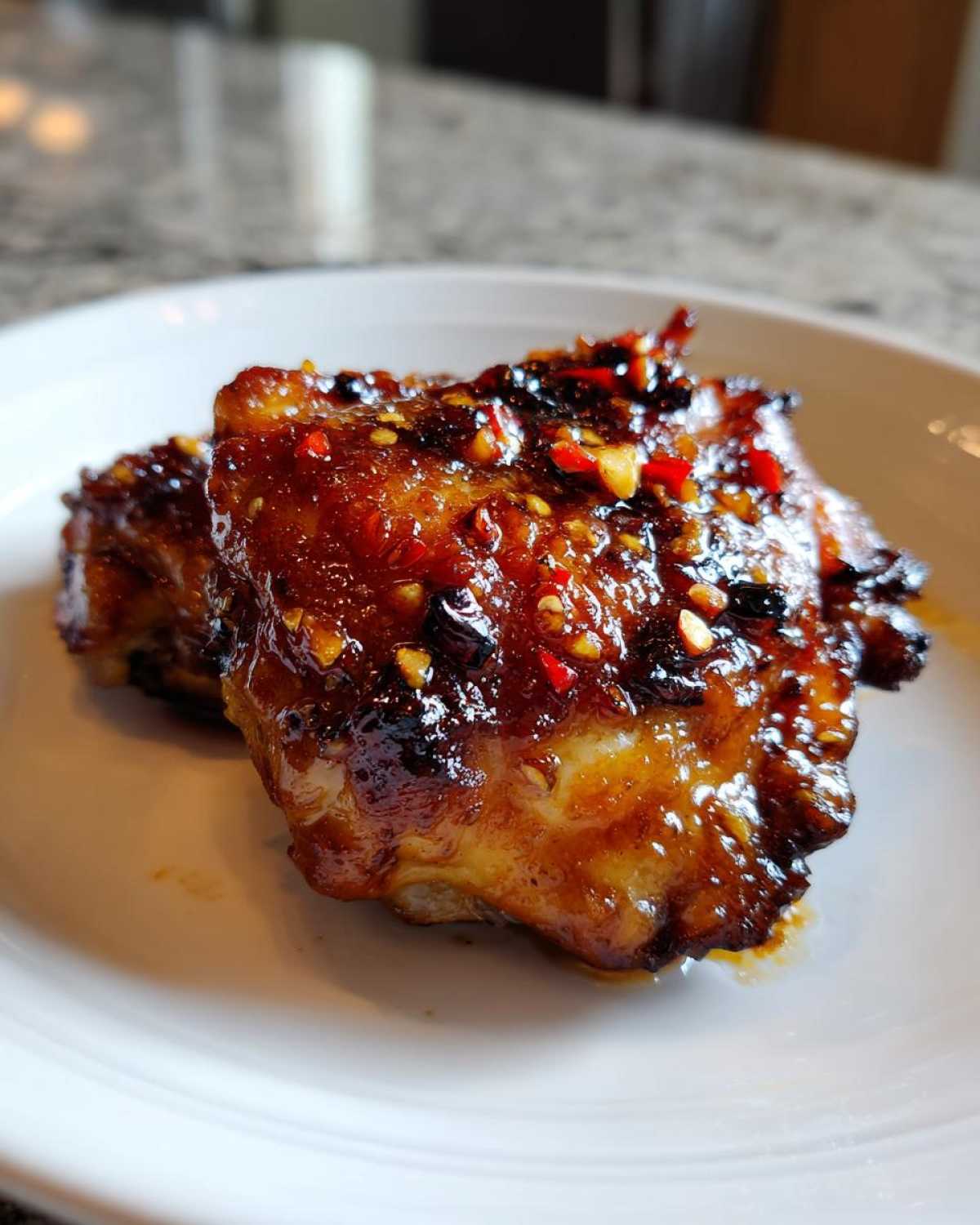 Close-up of two glistening Spicy Honey Garlic Air Fryer Chicken Thighs covered in a thick, dark glaze with visible red chili flakes.
