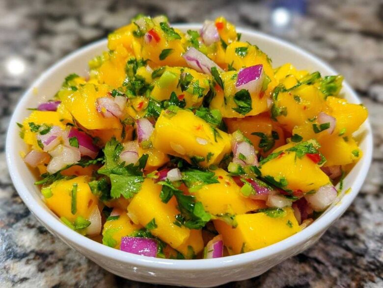 Close-up of a white bowl filled with bright yellow Spicy Mango Salsa, featuring diced mango, red onion, and cilantro.