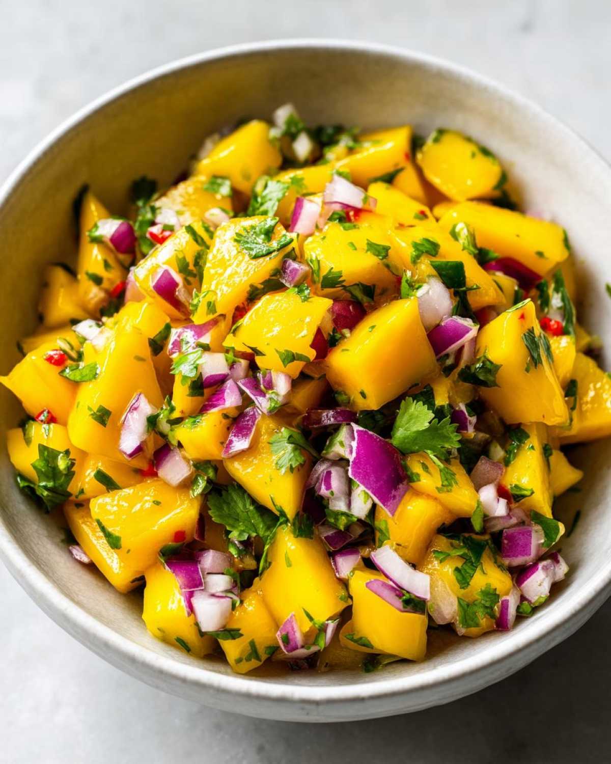 Close-up of bright yellow chunks of mango mixed with diced red onion and cilantro for Spicy Mango Salsa.