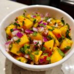 Close-up of bright yellow, diced mango mixed with chopped red onion and cilantro in a white bowl, showcasing the Spicy Mango Salsa.