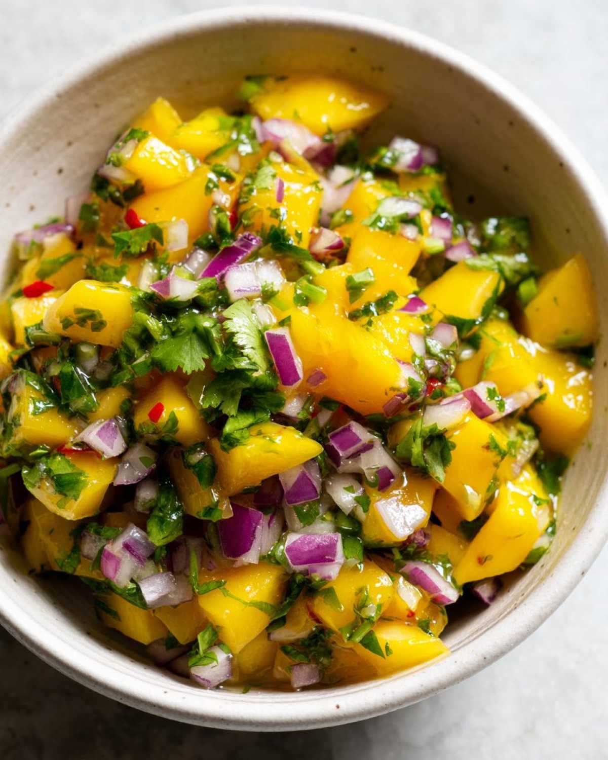 Close-up overhead shot of freshly made Spicy Mango Salsa featuring bright yellow mango chunks, diced red onion, and cilantro.