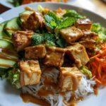 Close-up of a Spring Roll Bowl with Peanut Sauce featuring crispy tofu, vermicelli noodles, shredded carrots, cucumber, and mint.