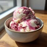 Two scoops of creamy Strawberry Banana Ice Cream swirled with bright pink berry puree in a light ceramic bowl.