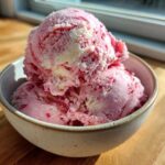 Three scoops of pink and white swirled Strawberry Banana Ice Cream in a speckled bowl.