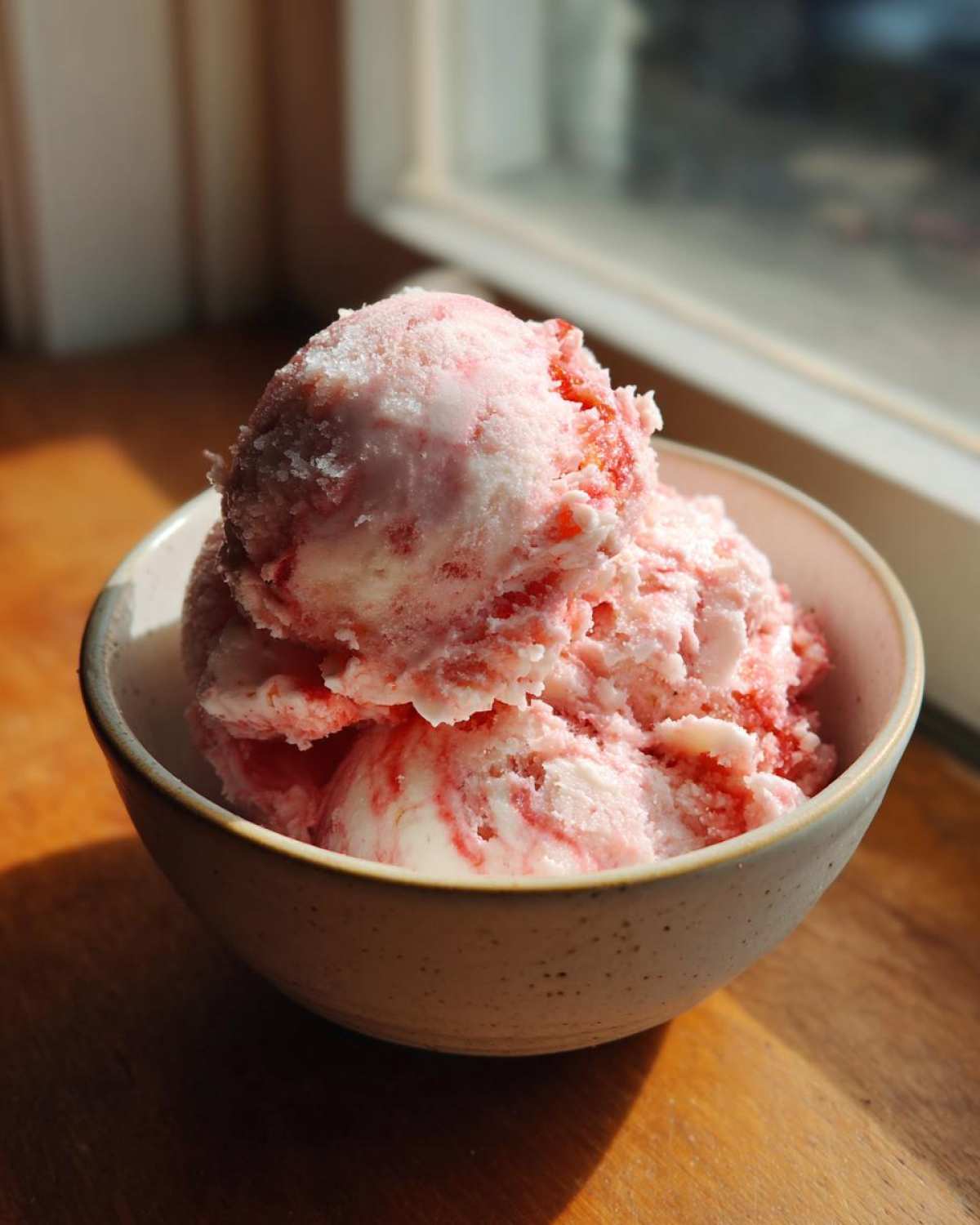 Three scoops of pink and white swirled Strawberry Banana Ice Cream in a speckled ceramic bowl.