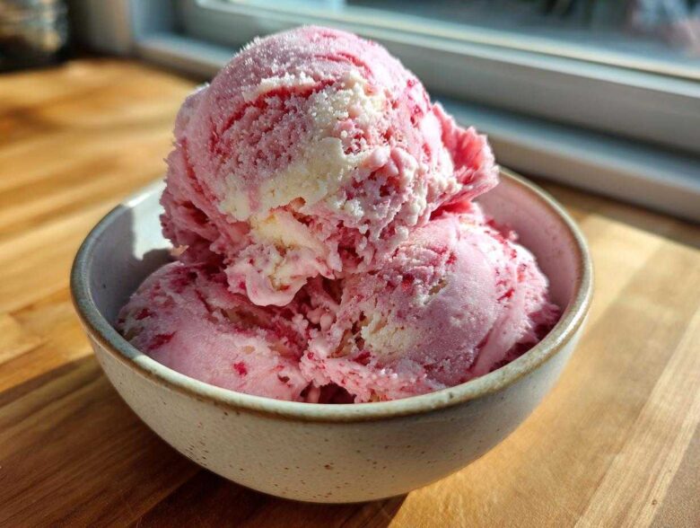 Three scoops of pink and white swirled Strawberry Banana Ice Cream in a speckled bowl.