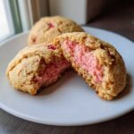 Close-up of a Strawberry Cheesecake Stuffed Cookie broken in half, revealing the bright pink, creamy filling.