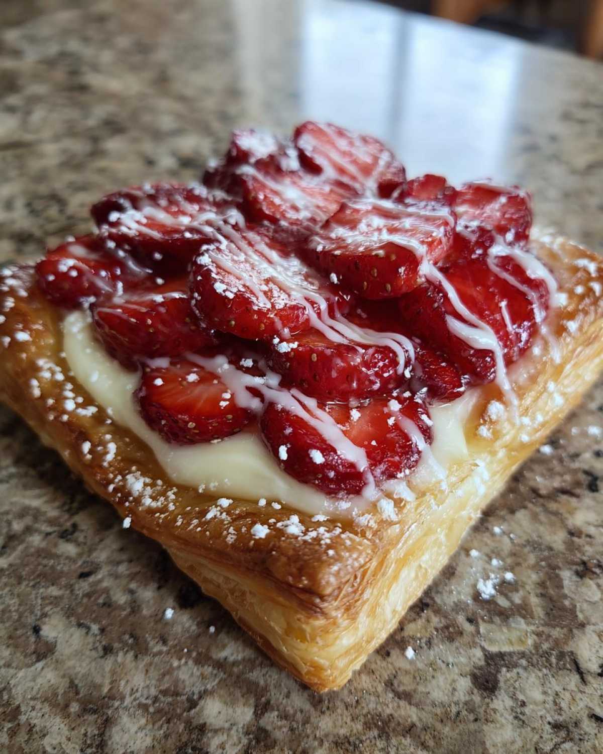 A close-up of a square Strawberry Cream Cheese Danish with fresh strawberries and white icing.