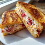 Two halves of golden-brown Strawberry Cream Cheese Stuffed French Toast showing the rich, creamy filling with visible strawberries.