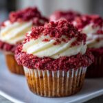 A close-up of a delicious Strawberry Crunch Cupcakes topped with white frosting and red crumble.