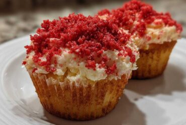 Two delicious Strawberry Crunch Cupcakes topped with white frosting and bright red crunchy crumbs.